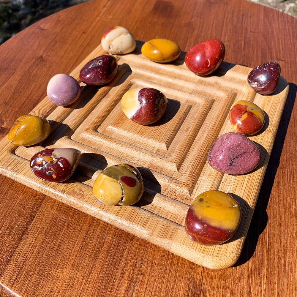Sixteen mookaite tumbled stones on a stepped wooden tray, ranging from cream and mustard to deep red and plum