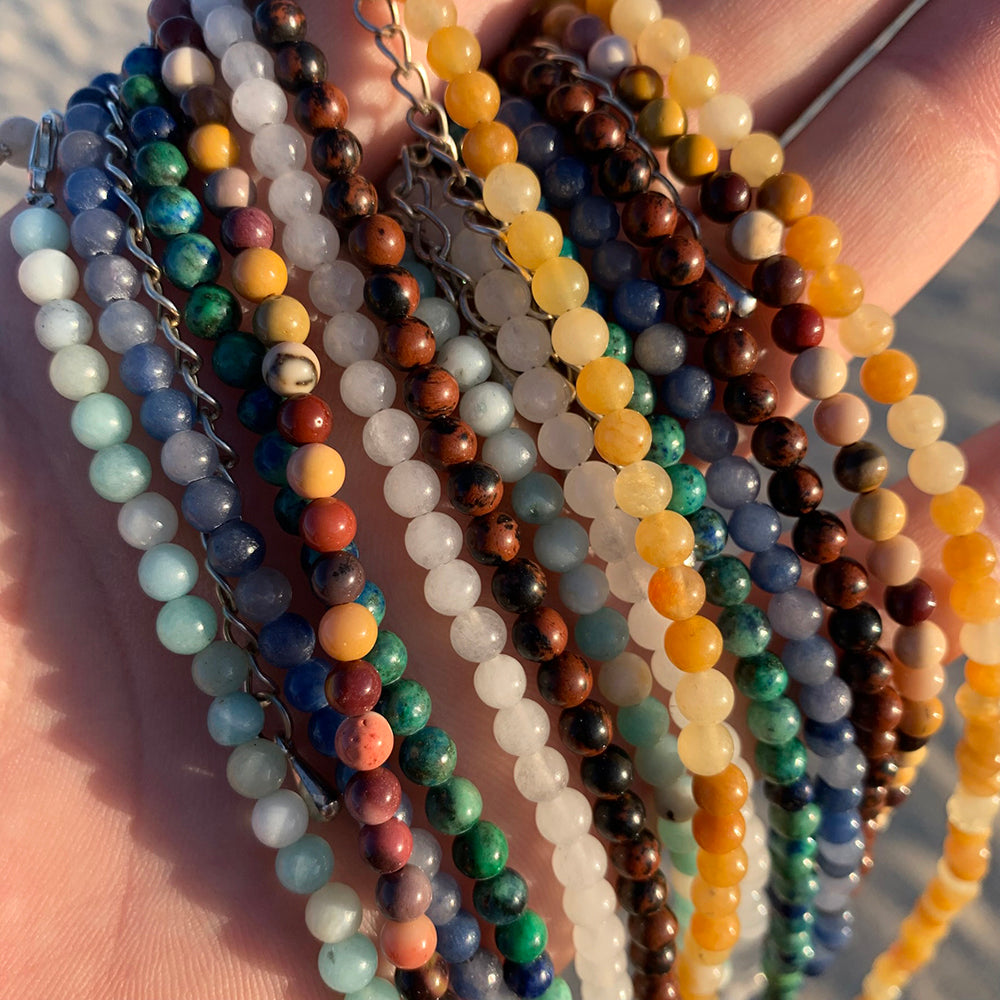Close-up of the seven beaded chakra necklaces held across an open palm, showing the round beads and silver clasp chains