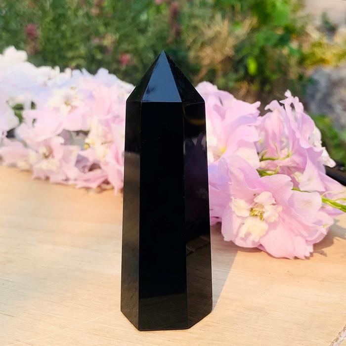 Six-sided black obsidian point standing beside pink flowers