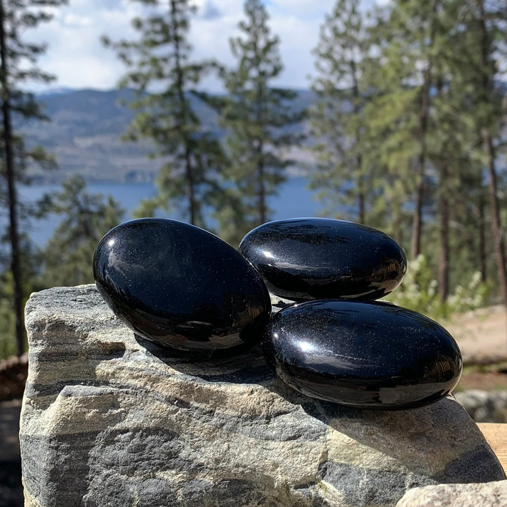 Three black obsidian palmstones shining in the sun on a rock above a mountain lake