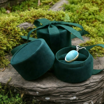 The larimar pendant resting in an open round green velvet jewelry box