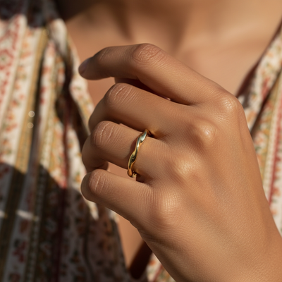 The gold wave ring worn on a finger, showing its slim, wavy band on the hand