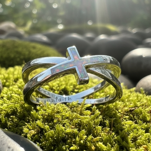 The opal cross ring on moss, its two crossing silver bands showing the word faith engraved inside