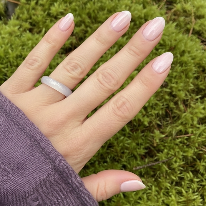 A smooth milky pink agate band worn on a finger against green moss