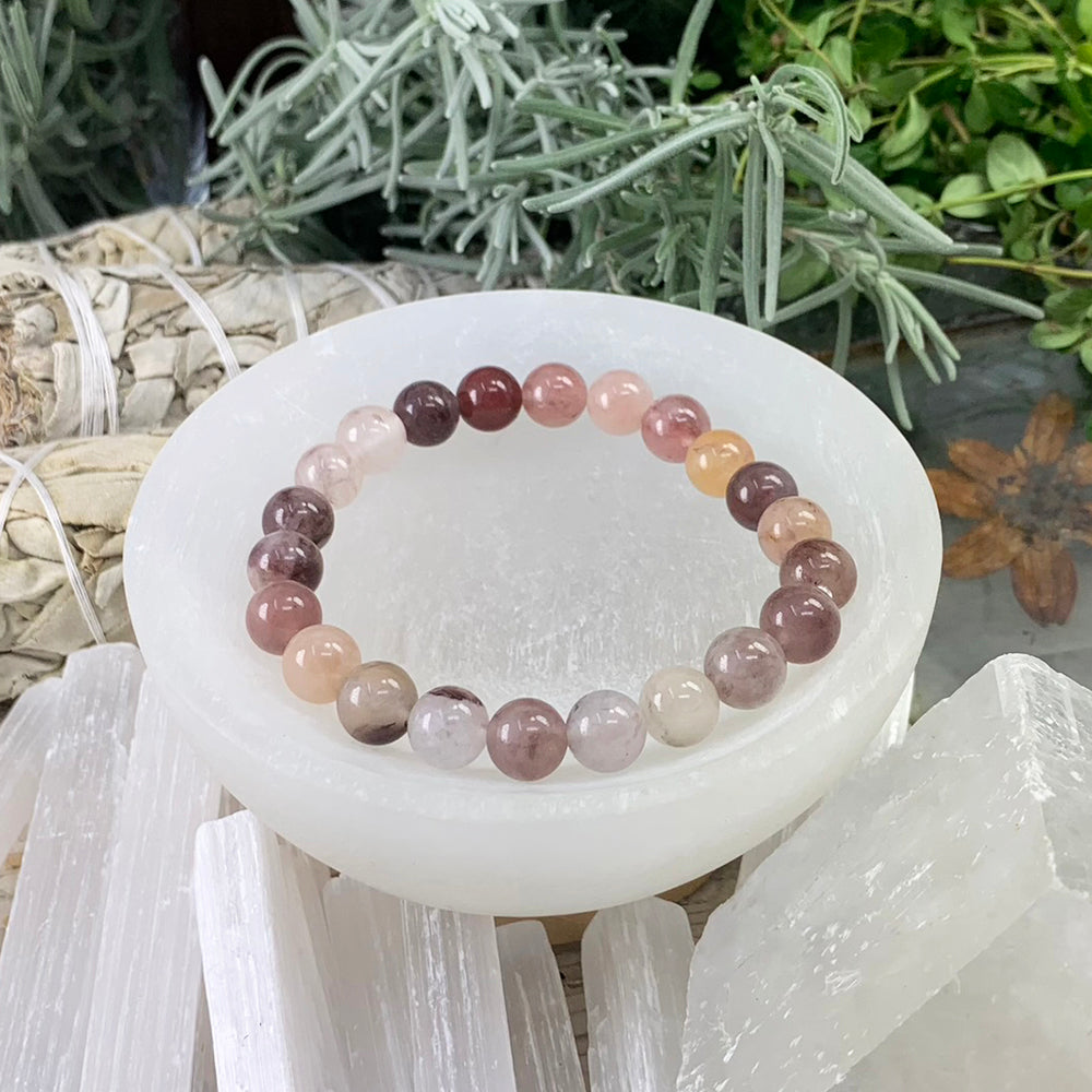 A purple aventurine bead bracelet in shades of plum, blush and cream resting in a white selenite bowl among selenite sticks and sage