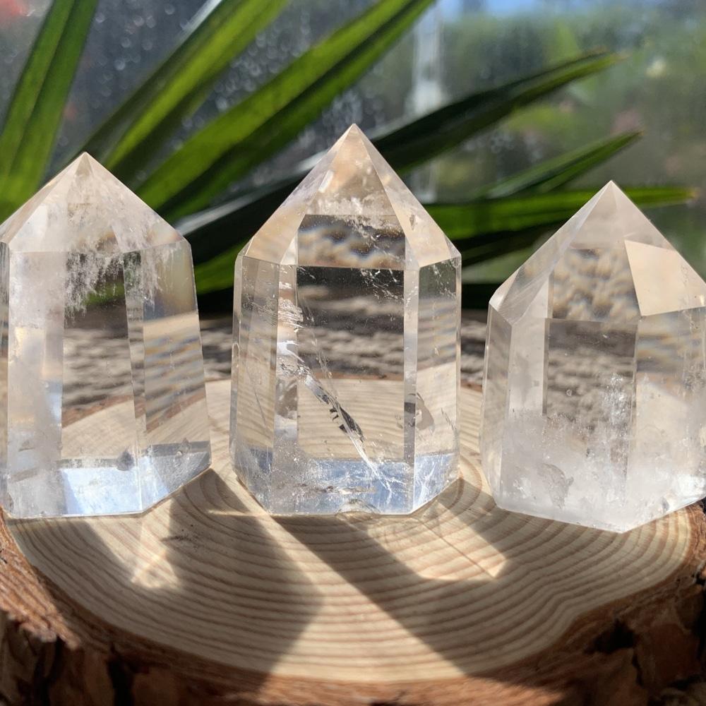 Three short clear quartz generators side by side on a wood slice, each with different clarity and veils