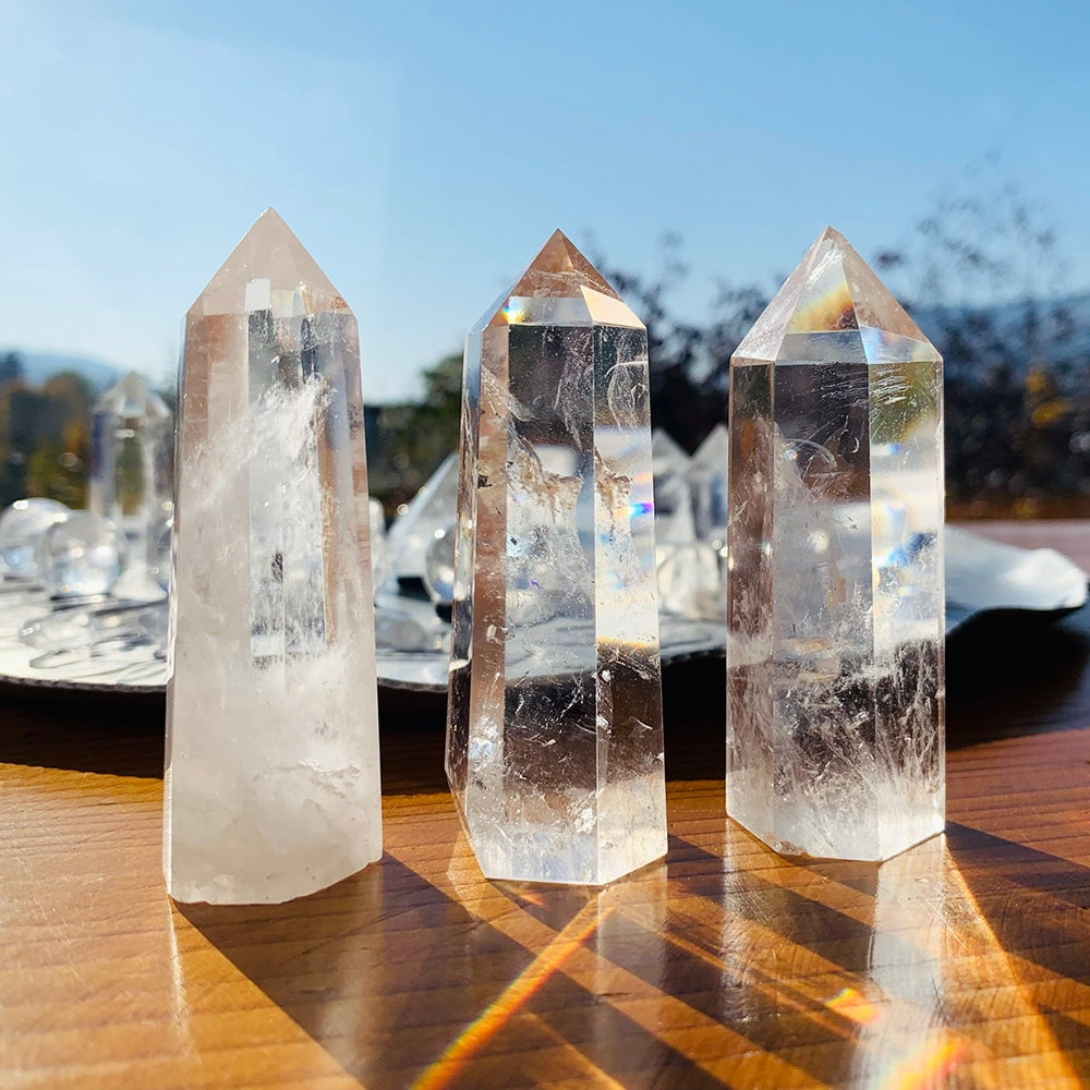 Three polished clear quartz points standing in bright sun on a wooden table, scattering small rainbows