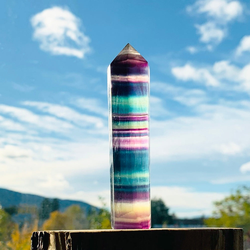 Rainbow fluorite point standing upright on its flat base on a wooden post under a blue sky