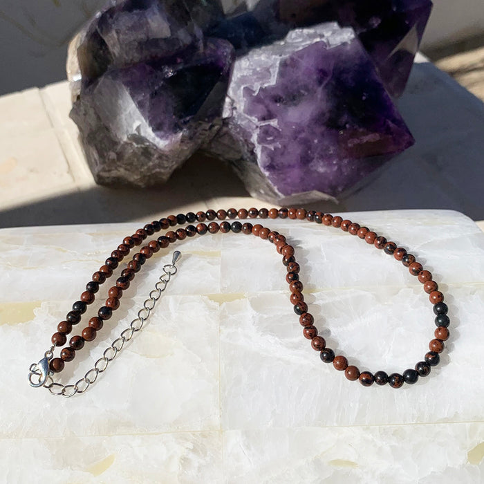 Red obsidian beaded necklace with a silver clasp chain on a selenite slab