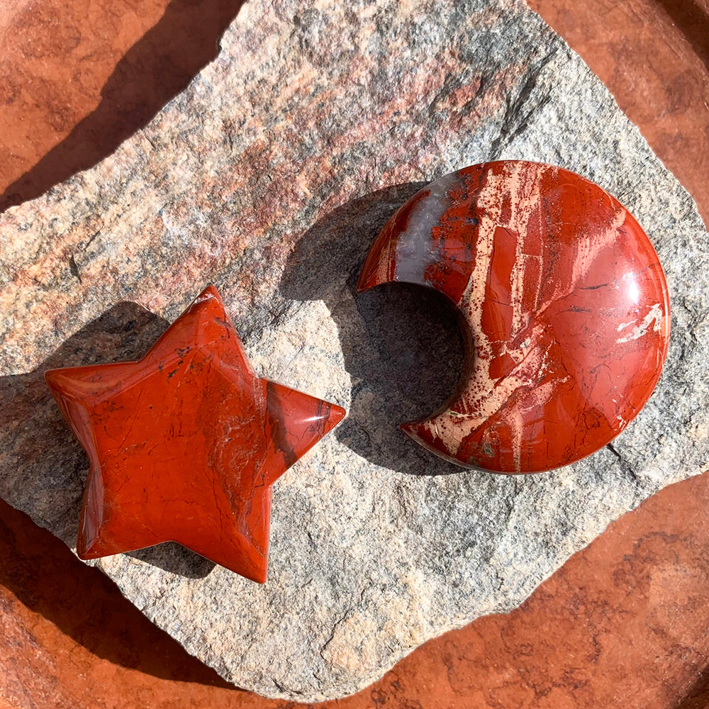 A polished red jasper star and crescent moon lying side by side on a slab of grey stone in the sun