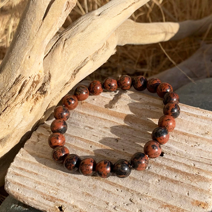 A bracelet of round mahogany-red obsidian beads with black markings on weathered wood