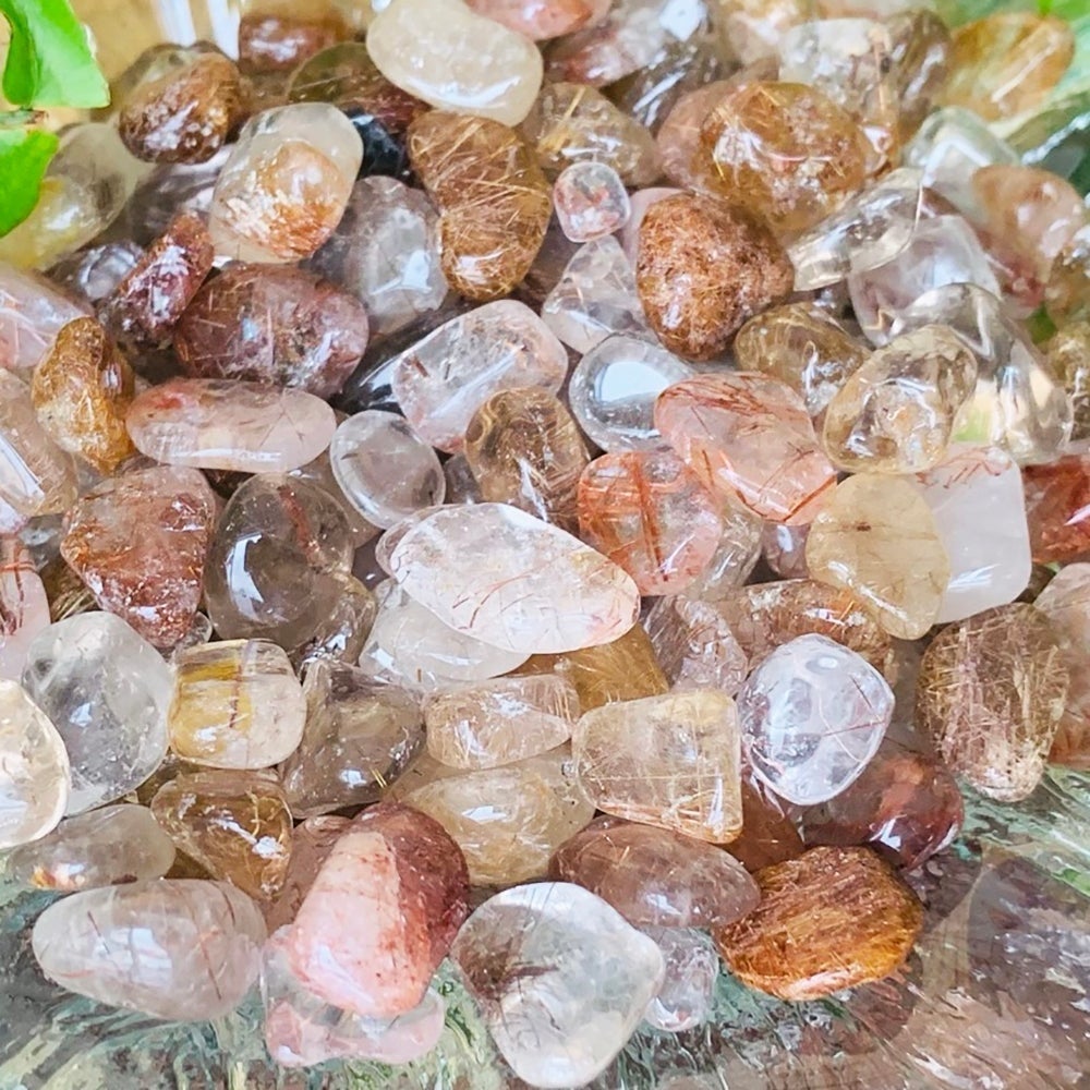 Close-up of tumbled rutilated quartz showing fine golden and red needle-like rutile strands inside clear and smoky quartz