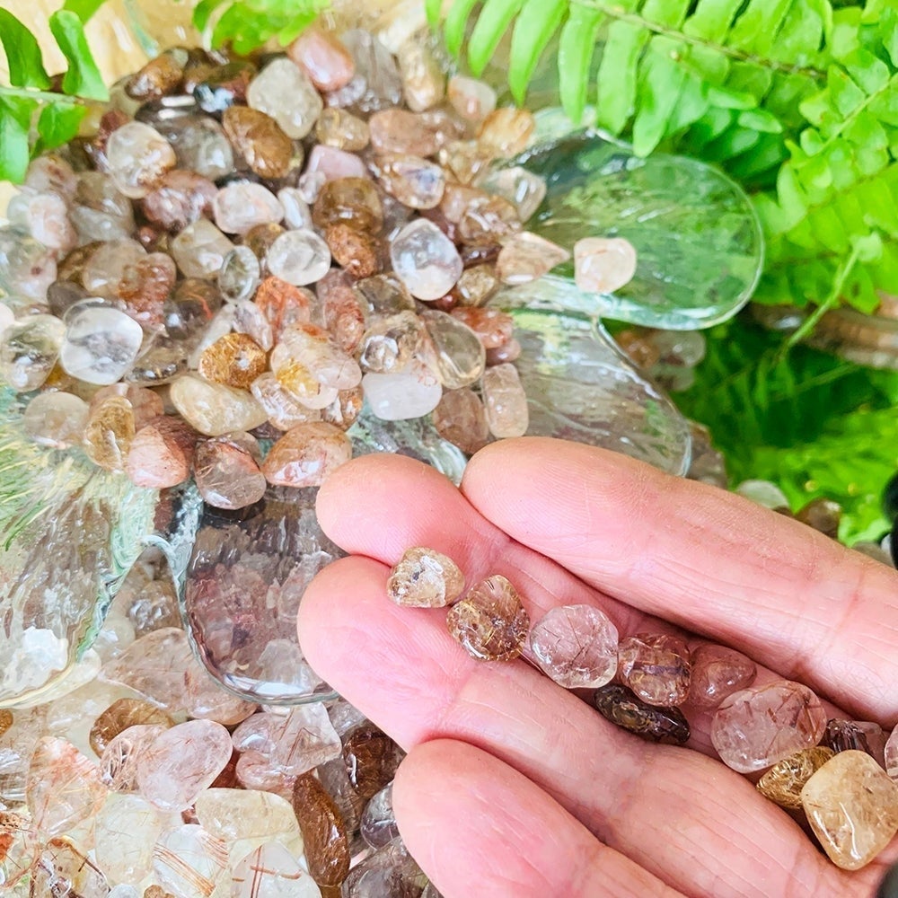 A row of small tumbled rutilated quartz pieces resting on fingers above a glass dish piled with more