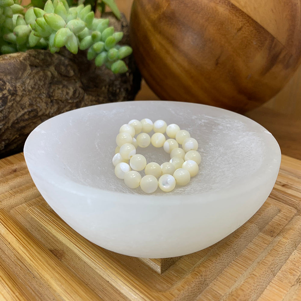 Selenite bowl on a wooden board with a white bead bracelet resting inside it