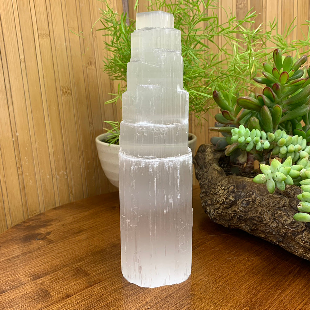The tiered selenite tower standing on a wooden table beside potted plants and succulents