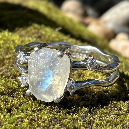 Close view of the moonstone ring on moss, showing the four-claw setting, split silver band and 925 stamp inside the band