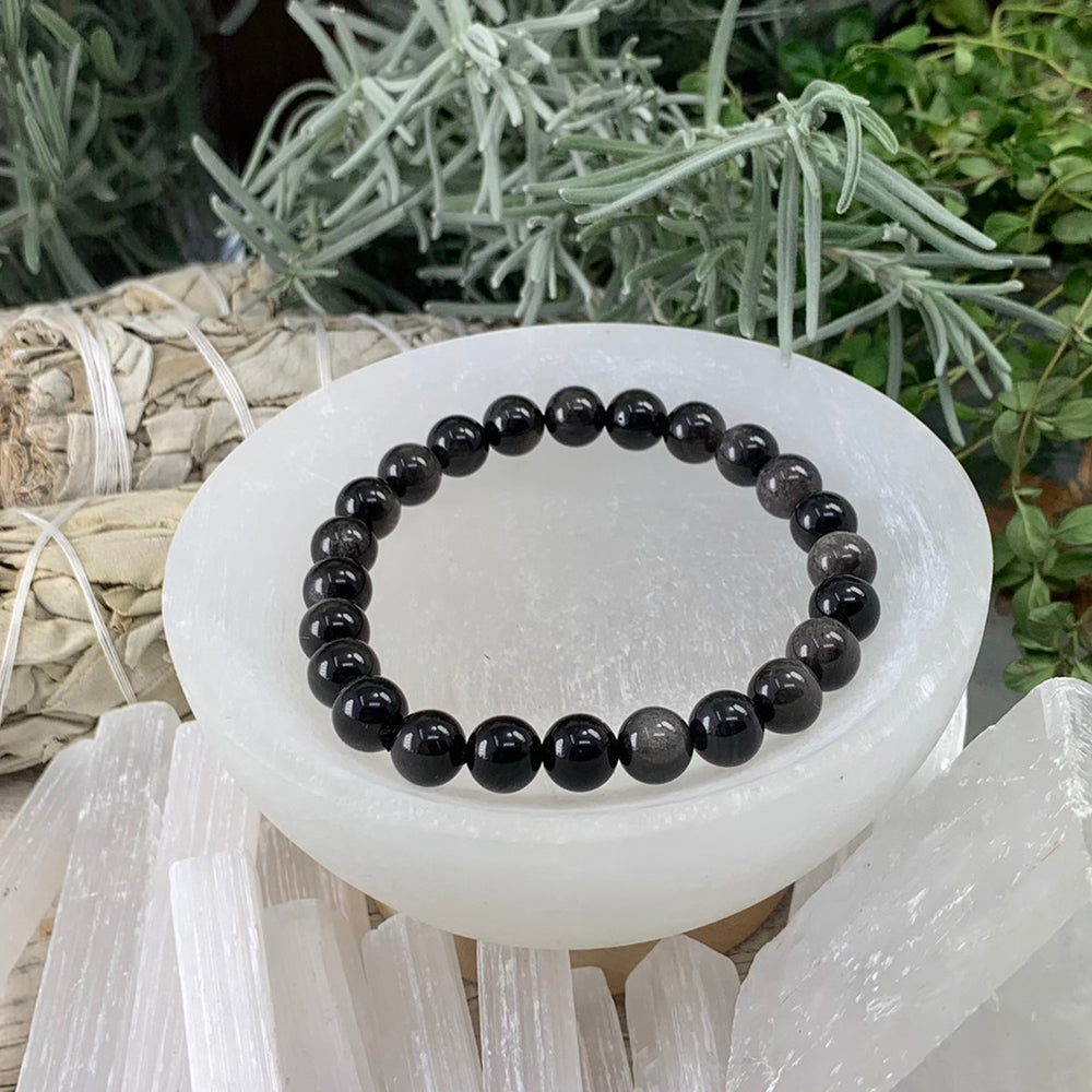 Silver Obsidian bead bracelet in glossy black beads with a silvery sheen, resting in a white selenite bowl