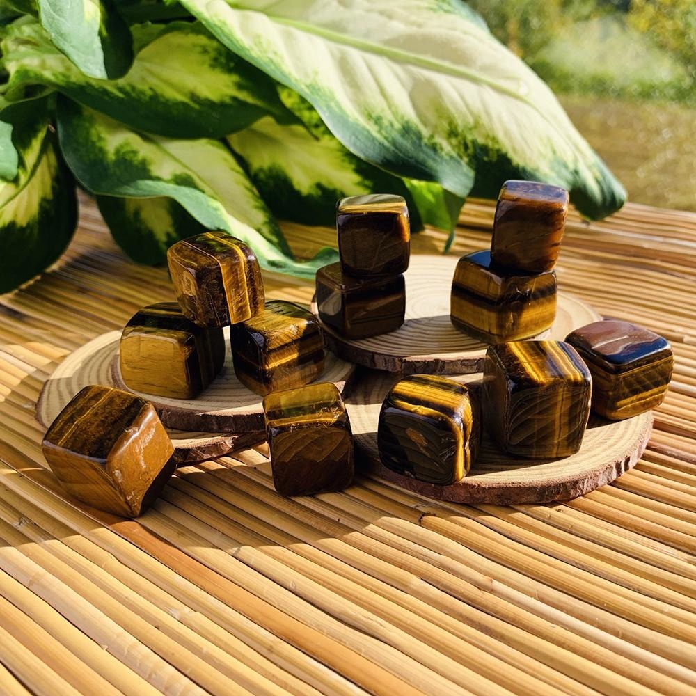 Several tiger’s eye tumbled cubes on wooden slices in sunlight, their golden bands catching the light