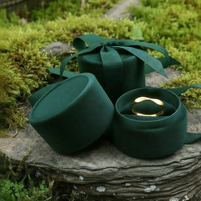 A soft round green velvet jewelry box open on a mossy stone, a gold ring resting inside