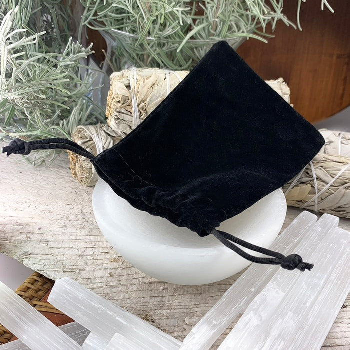 Black velvet drawstring pouch resting on a white bowl beside selenite sticks