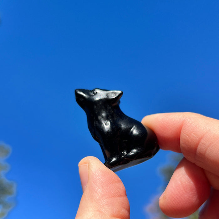 Small seated black agate wolf held between thumb and fingers against a blue sky